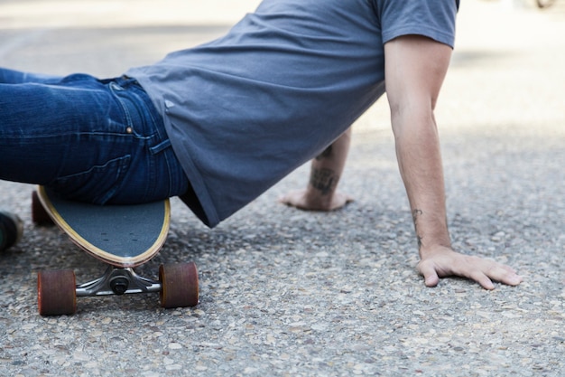 Crop man sitting on longboard on pavement