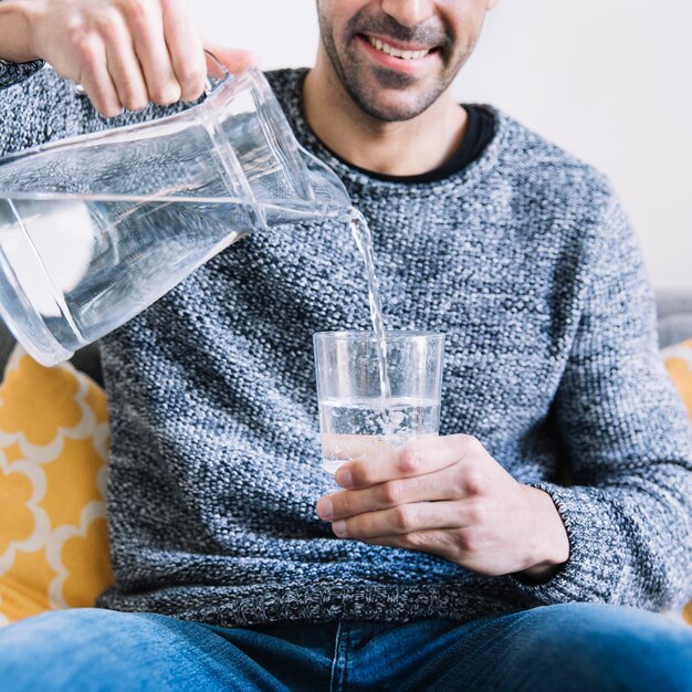 Crop man on sofa pouring water