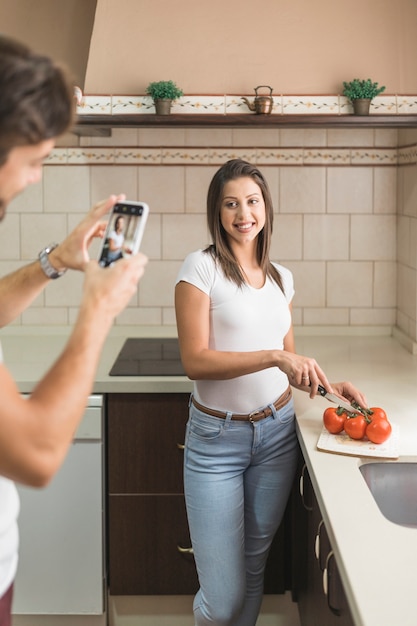 Crop man taking picture of cooking woman in kitchen