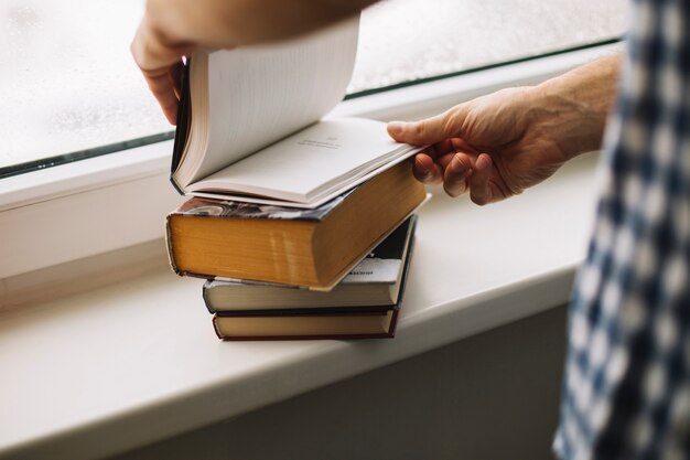 Crop man thumbing books near window