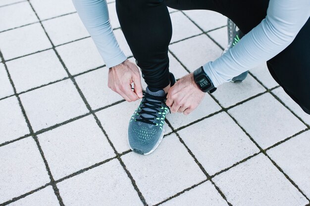 Crop man tying laces on sneakers