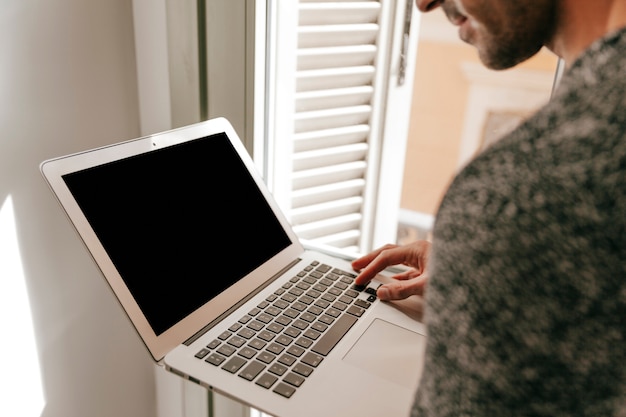 Crop man using laptop near window