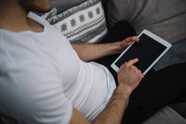 Crop man using tablet on sofa