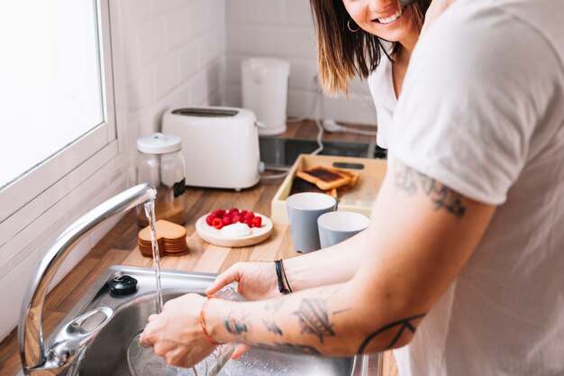 Crop man washing dishes near woman