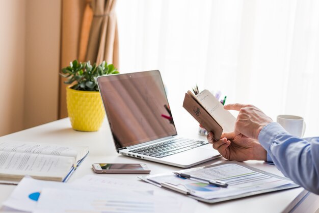 Crop man with notebook near laptop