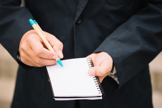 Crop man writing in blank notebook