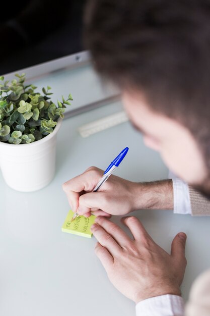 Crop man writing on sticky note