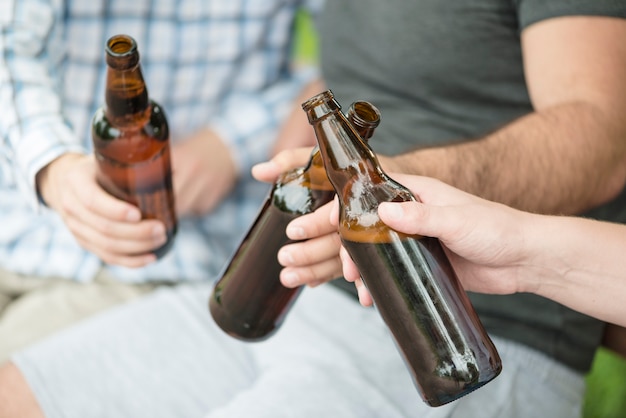 Crop men clinking bottles on bench