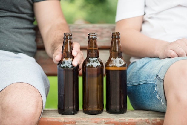 Free photo crop men sitting on bench near beer