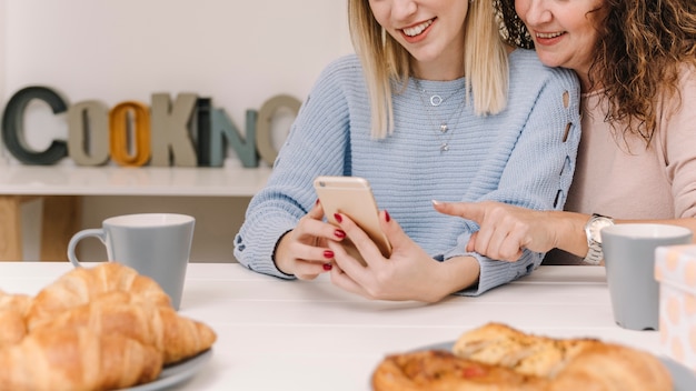 Crop mother and daughter using smartphone during breakfast