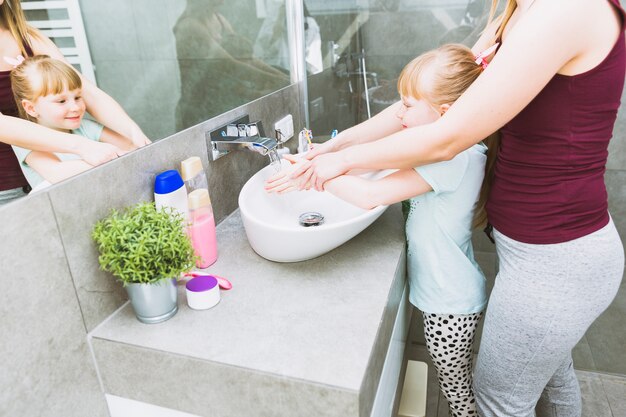 Массовая мать помогает дочери мыть руки