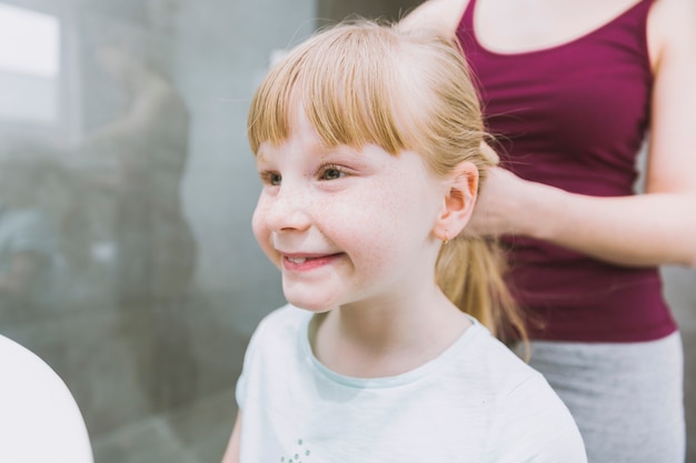 Crop madre che fissa i capelli della ragazza sorridente