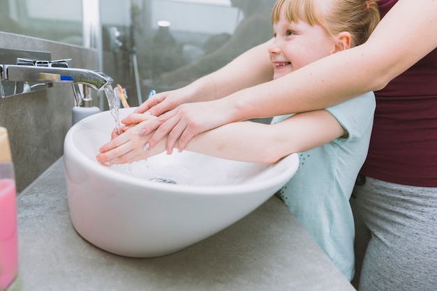 Crop mother washing hands of cheerful daughter