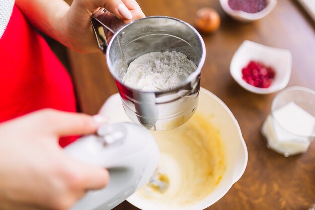 Crop person bolting flour and mixing batter