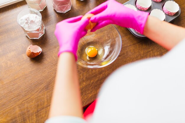 Crop person breaking eggs into bowl