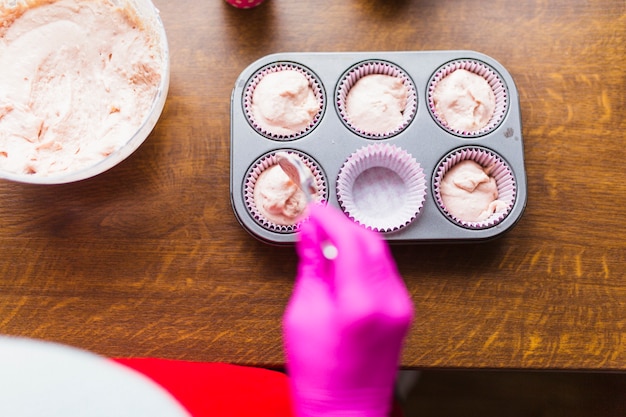 Crop person filling paper cups with batter