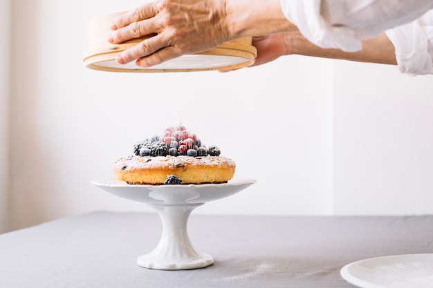 Crop person powdering biscuit with berries