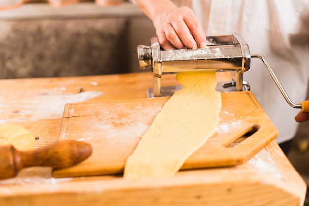 Crop person rolling dough on pasta maker