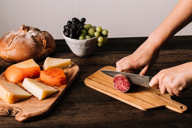 Crop person slicing sausage near food