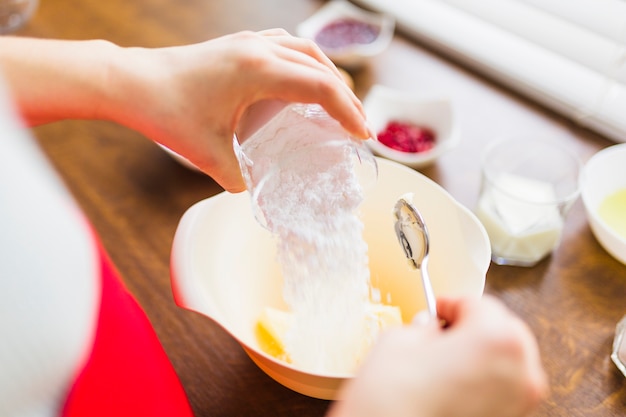 Crop person spilling flour into bowl