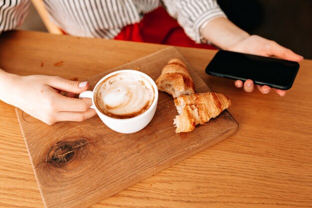 Обрезайте фотографию чашки с кофе и французскими круассанами на столе на деревянном столе.