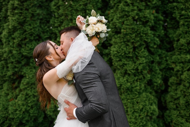 Free photo crop portrait of loving brides couple kissing and hugging while standing in the garden beautiful brode girl with curly hairstyle in wedding dress with groom in suit wedding day tenderness moment