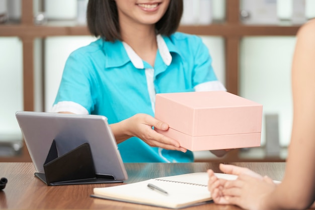 Crop receptionist giving beauty box to client