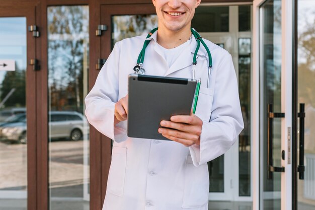 Crop smiling medic with tablet at hospital