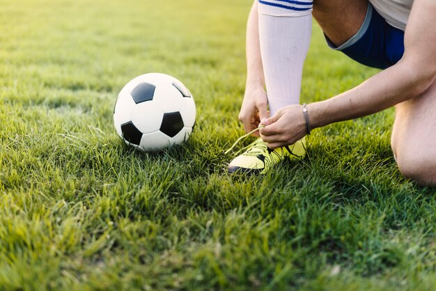 Crop sportsman tying laces on field