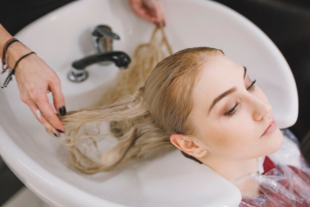 Crop stylist washing hair of blonde