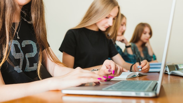 Crop teen using laptop near friends