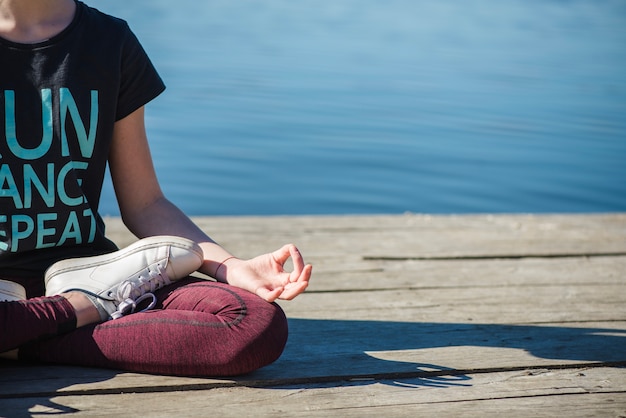 Crop teenager meditating on pier