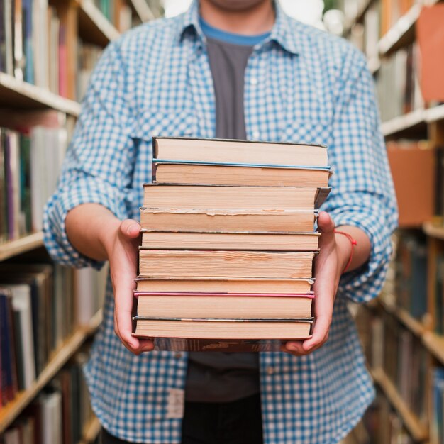 Crop teenager showing pile of books