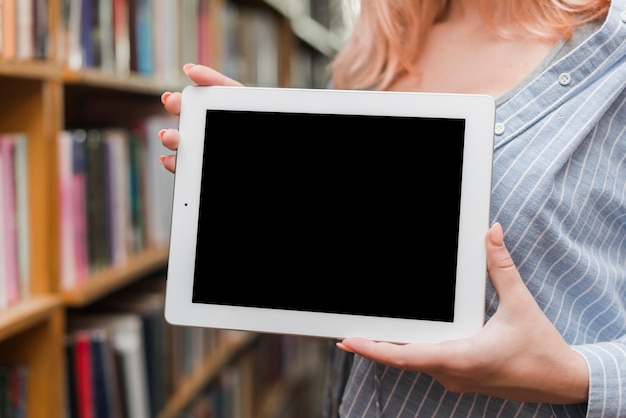 Crop teenager showing tablet in library