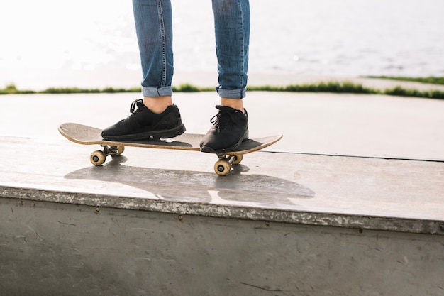 Crop teenager standing on skateboard on border