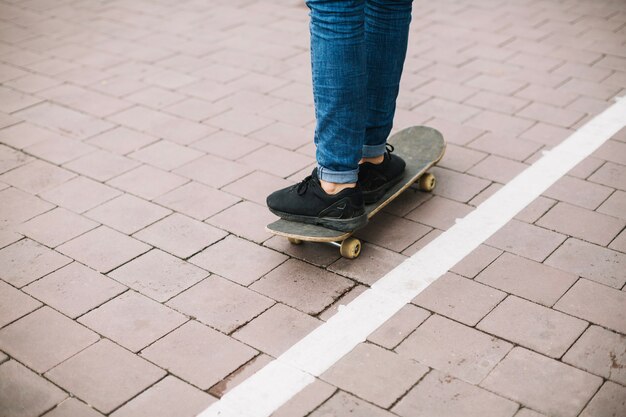 Crop teenager standing on skateboard