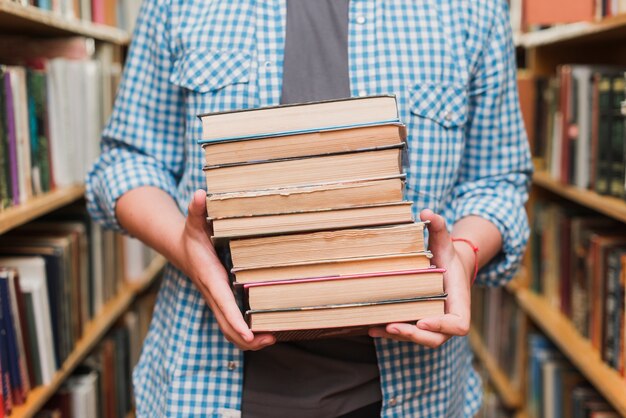 Crop teenager with books between bookshelves