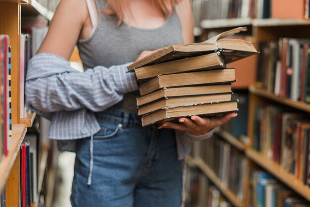 Crop teenager with stack of old books