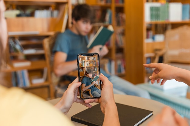 Crop teenagers making photo of friend in library