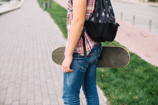 Crop teeneger carrying skateboard