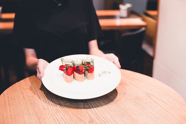 Crop waitress holding plate with open sandwiches