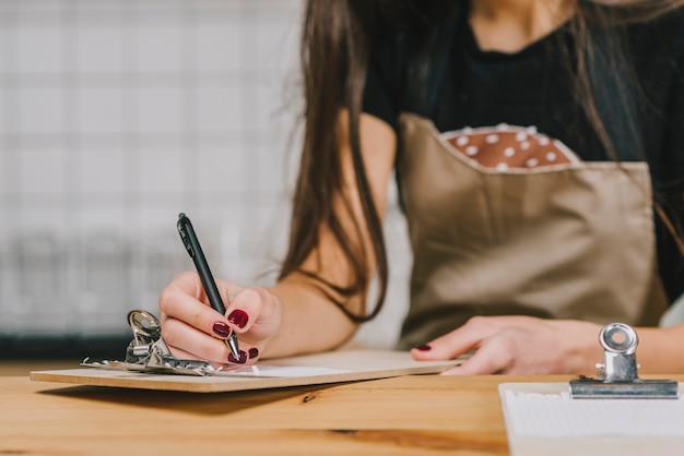 Crop waitress writing on clipboard