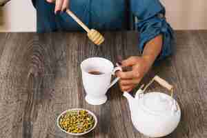 Foto gratuita raccolga la donna che aggiunge il miele a tè
