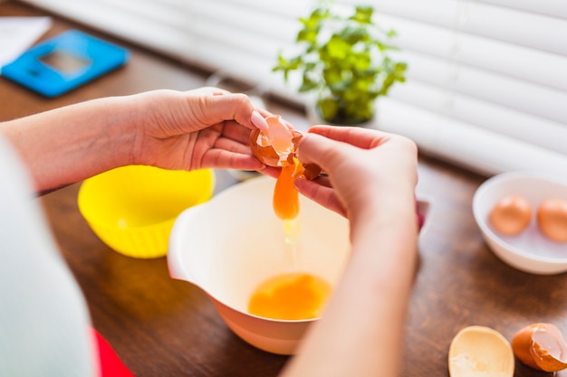 Crop woman breaking eggs into bowl