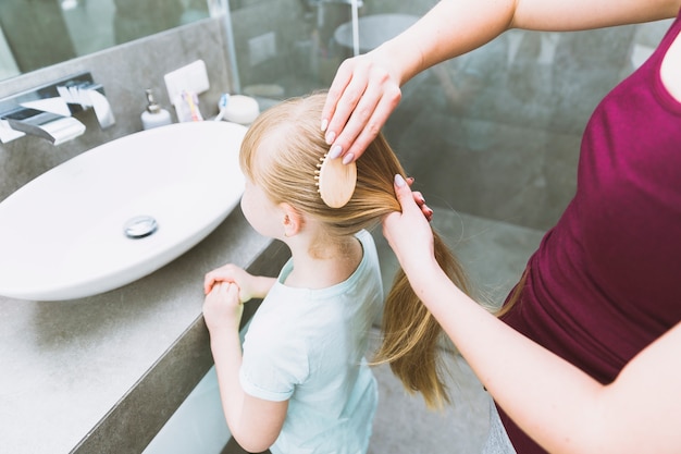 Crop woman brushing daughter for ponytail