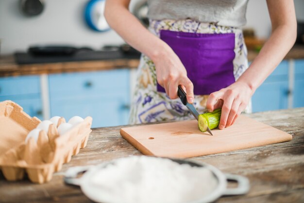 Crop woman cutting cucumber