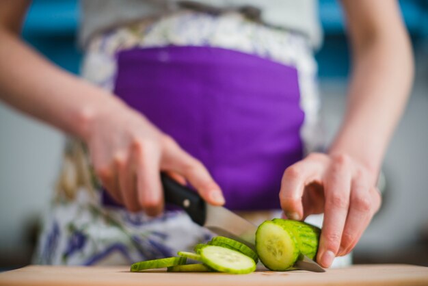 Crop woman cutting fresh cucumber