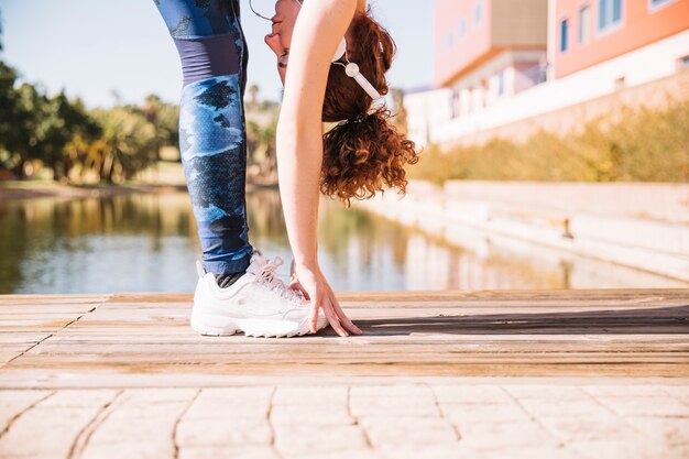 Crop woman doing bending exercise on pier