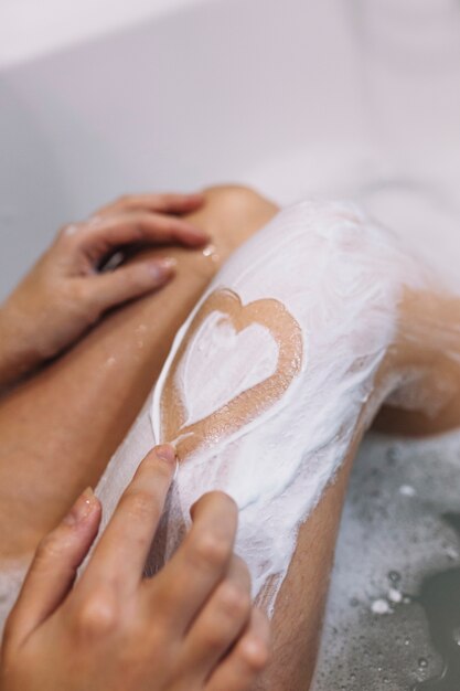 Crop woman drawing heart on leg