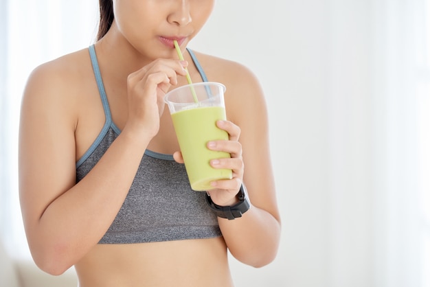 Crop woman drinking green smoothie